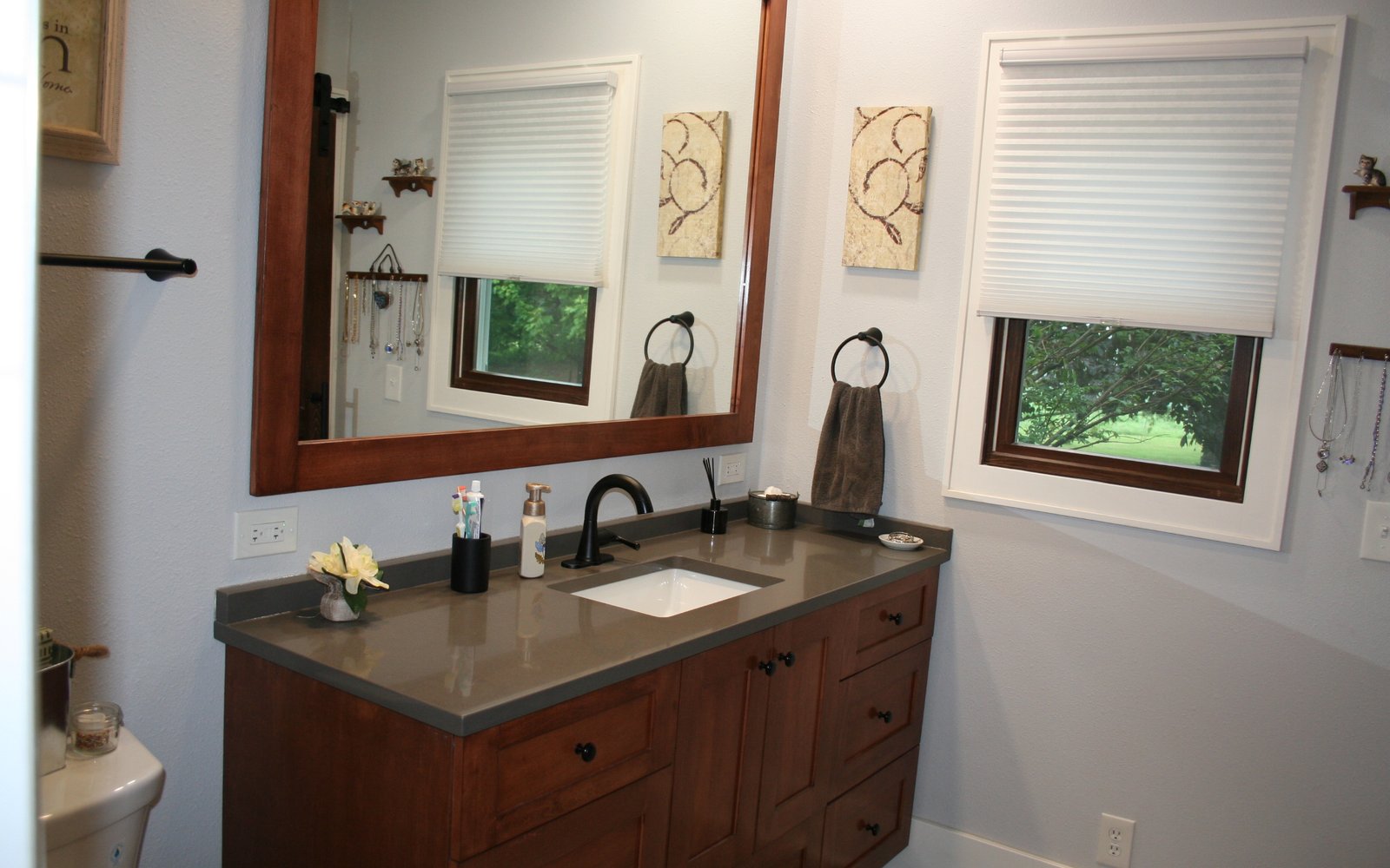 Warm wood bathroom vanity with drawers, a gray counter, and a framed mirror