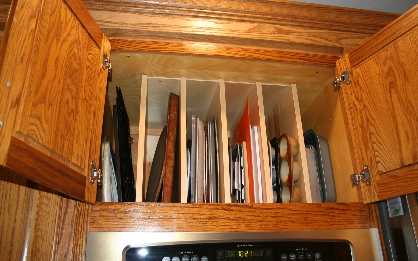 Custom pull-out tray dividers installed in an oak cabinet above a kitchen range