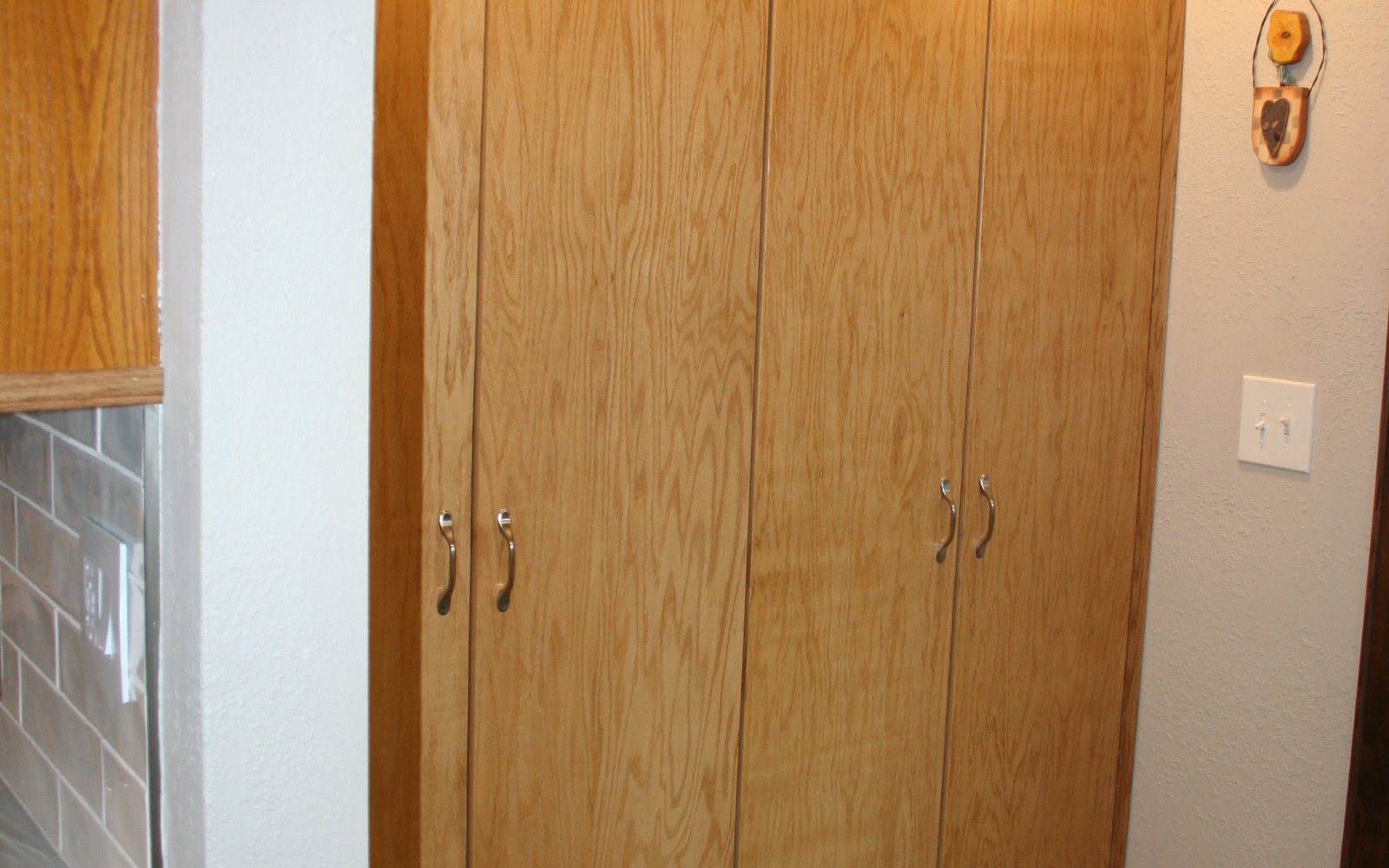 Tall light oak storage cabinets fitted closely between adjacent walls