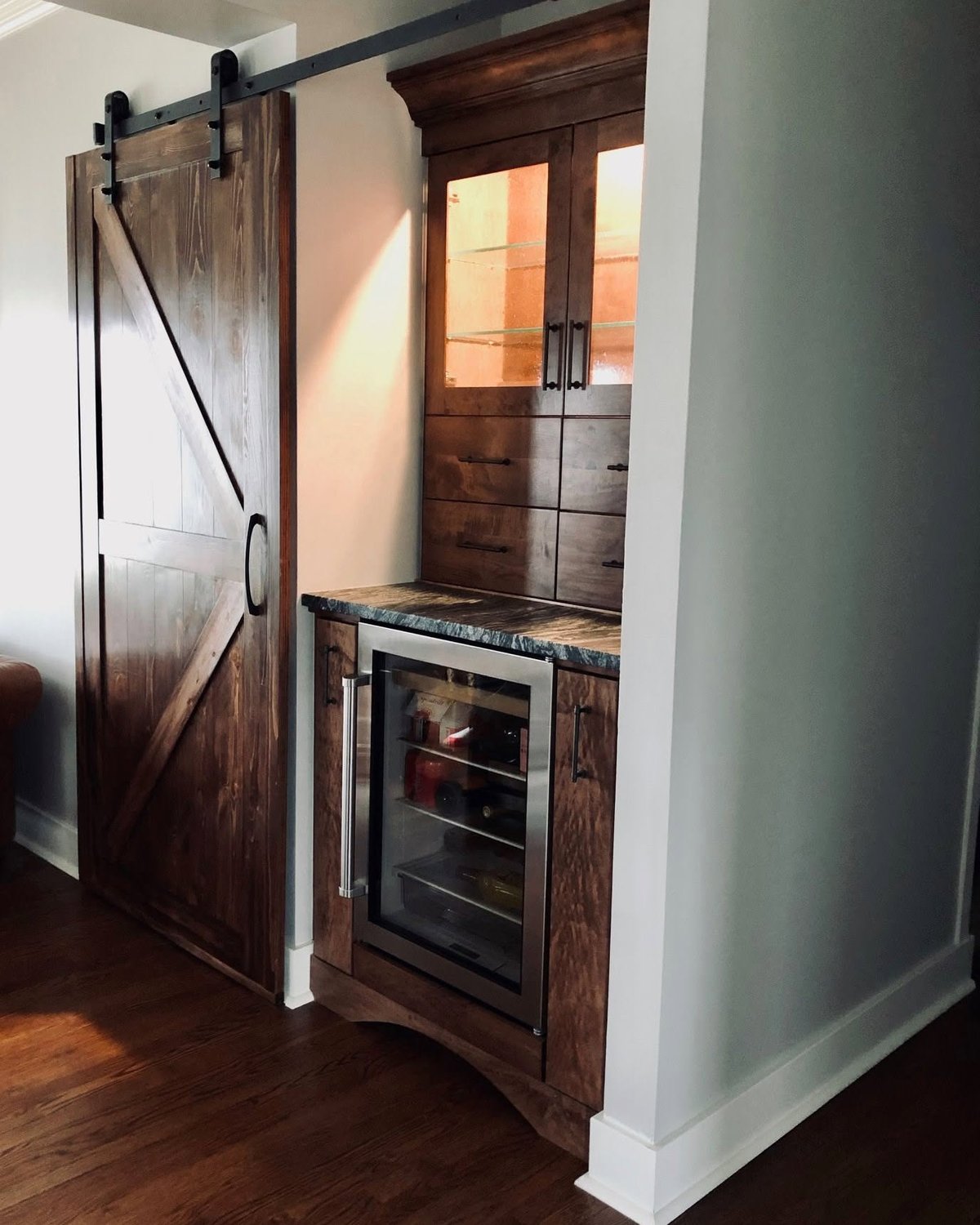 Stained sliding barn door beside a matching beverage cabinet and integrated cooler