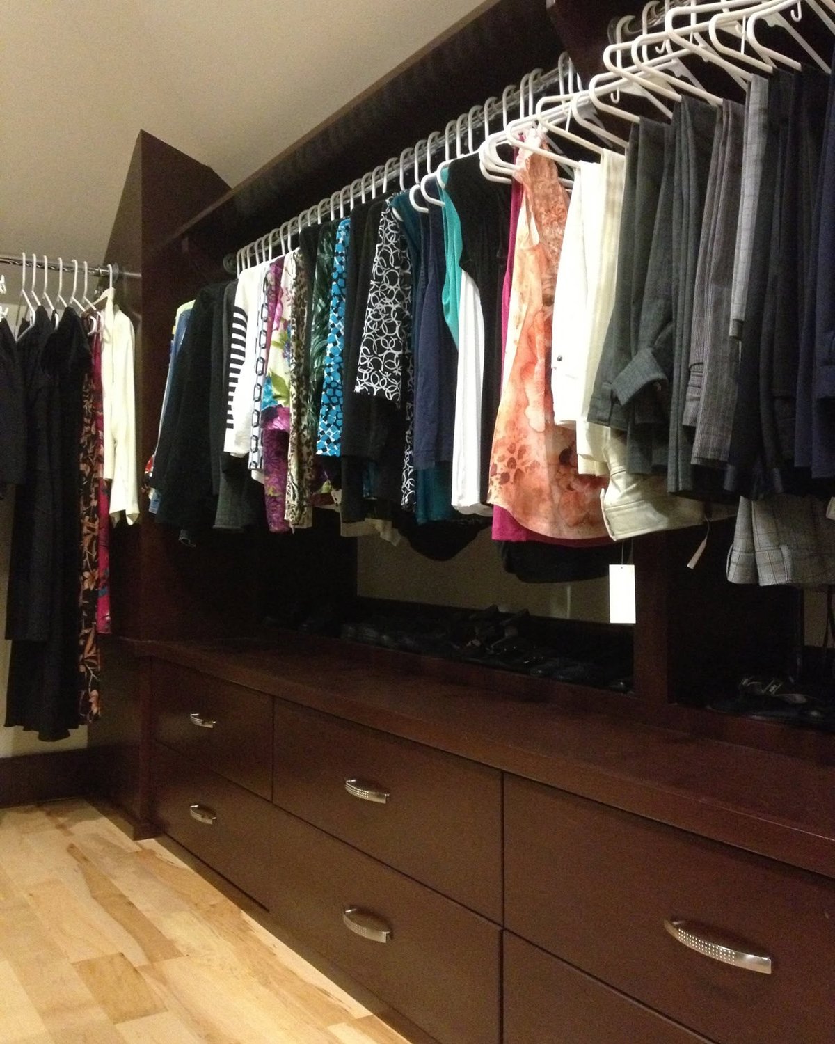 Walk-in closet with custom dark wood drawers, shelving, and hanging storage