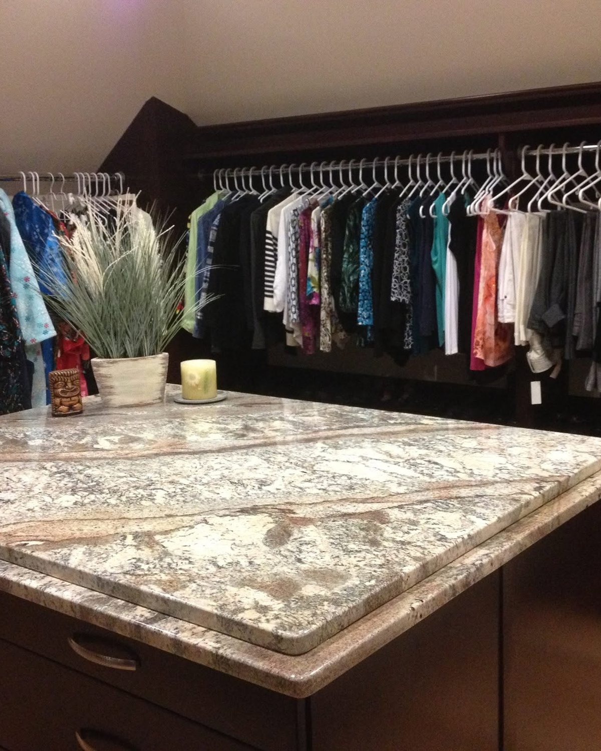 Dark wood walk-in storage with fitted shelving, drawers, hanging space, and a stone-topped island