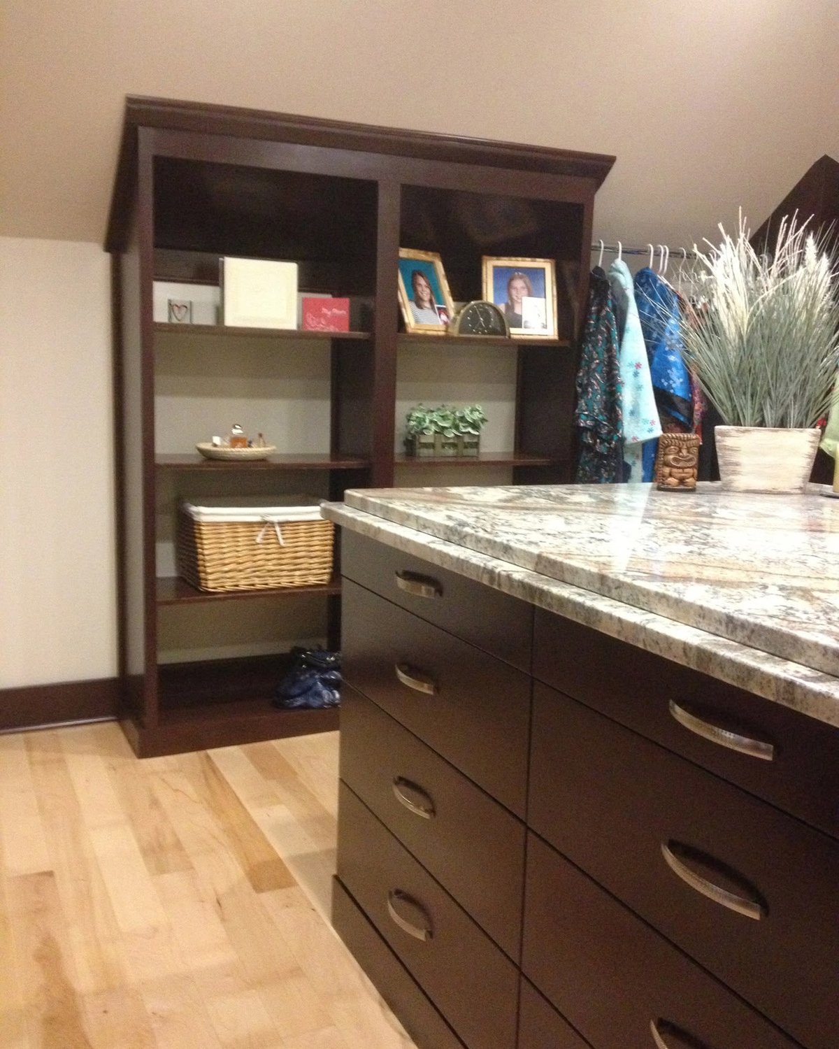 Custom dark wood closet with shelving, drawers, hanging space, and a stone-topped island