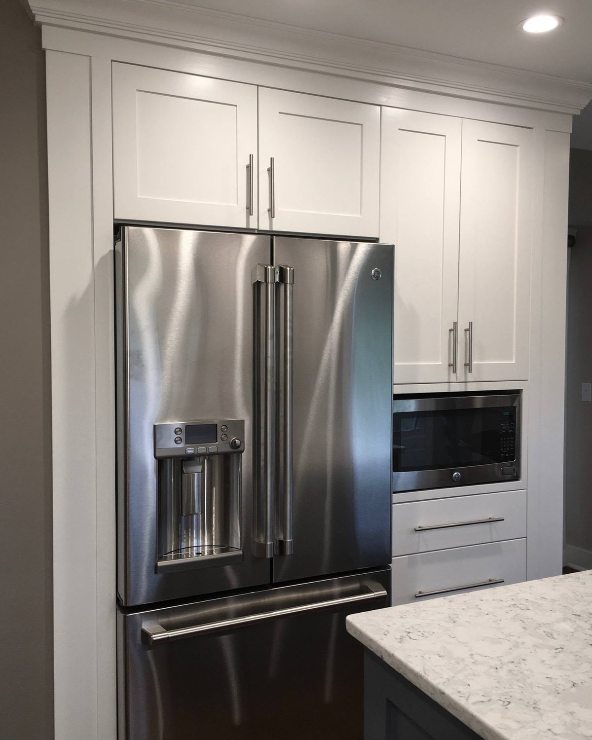White full-height kitchen cabinetry fitted around a refrigerator and built-in appliance