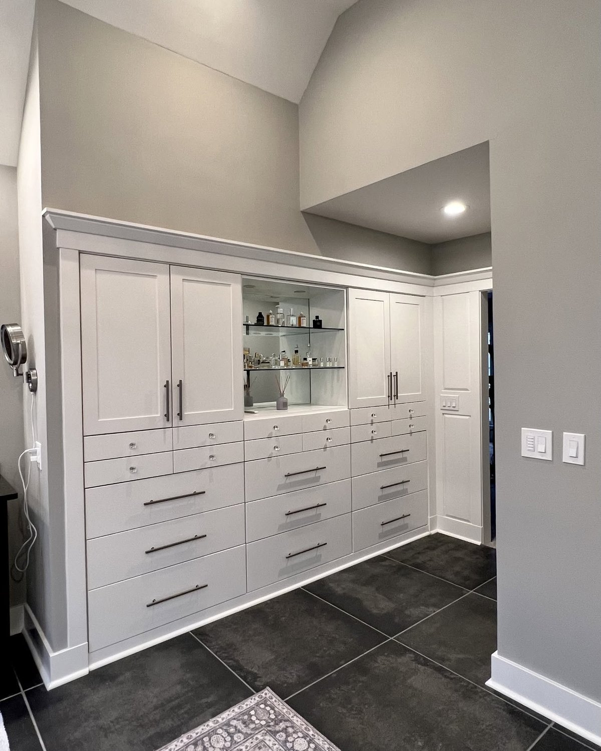Floor-to-ceiling white storage cabinetry with drawers and a central glass display section